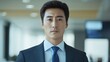 © STwul - Confident Asian businessman in suit, serious expression, office background.