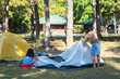 © Pornpimon - Mother and daughter are helping each other set up a tent in nature on a sunny day. Family camping in the woods on summer vacation