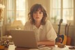 © Peeradontax - A woman in her 30s sits at a desk with a laptop, surrounded by warm lighting and artistic decor.