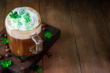 Tasty delicious irish coffee in glass, with whipped cream, green sugar sprinkles and shamrock decor, on wooden bar table with coffee beans, lucky clover leaves, festive coffee drink for Patricks day