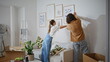 © stockbusters - Couple hanging pictures wall apartment. Happy woman and man enjoy collaborating