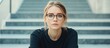 © The 2R Artificiality - Concentrated young Caucasian woman in glasses sitting on office building stairs contemplating her freelance career in natural light with copyspace