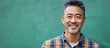 © The 2R Artificiality - Smiling 40-year-old Asian man in plaid shirt standing against vibrant green background with ample copyspace for text and design elements