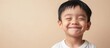© The 2R Artificiality - Happy Asian baby boy smiling widely in a close-up shot, with warm facial features and a playful expression, against a soft beige background, portrait, children, joy, copyspace for text.