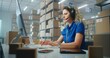 © Framestock - Female logistics coordinator wearing headset chats with customer on call, uses computer, works in post office or E-commerce store storage. Sorting center workers carrying cardboard boxes for delivery.