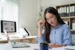 © Tj - Young Asian businesswoman wearing glasses and holding a pen, reviewing financial documents at her desk with a laptop and charts in a corporate setting