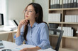 © Tj - Young Asian businesswoman wearing glasses, deep in thought while holding a pen, is diligently working with documents and a laptop at her office desk, embodying professionalism and focus