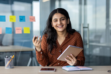 Wall Mural - Webcam view, online video meeting business conference. Young woman with notebook in hands looks into camera, smiles happily, listens to mentor, works inside office