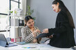 © amnaj - Two smiling Asian businesswomen reviewing and signing a contract together in a modern office, showcasing teamwork and collaboration