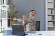 © amnaj - Happy businesswoman is stretching her arms while sitting at her desk in a modern office, taking a break from work and enjoying a moment of relaxation