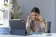 © amnaj - Young frustrated Asian businesswoman touching her head, suffering from headache, working on a digital tablet at her desk in office