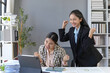 © amnaj - Two Asian businesswomen celebrating their success while engaging with a tablet in a sleek, modern office environment