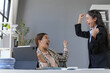 © amnaj - Two euphoric businesswomen are celebrating a successful project, expressing joy and excitement in their modern office workspace
