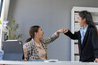 © amnaj - Two excited businesswomen celebrating a corporate victory with a fist bump in the office, showcasing teamwork and professional achievement