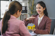 © amnaj - Smiling real estate agent holding a scale model house and presenting it to a client during a business meeting in the office