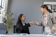 © amnaj - Two cheerful businesswomen shaking hands after reaching an agreement during a meeting in the office