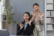 © amnaj - Two cheerful asian businesswomen showing ok sign with fingers and winking, expressing approval and satisfaction in workplace