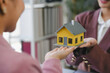 © amnaj - Real estate agent holding scale model house presenting to client in office during business meeting