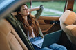 © SHOTPRIME STUDIO - Relaxed young woman in car using laptop, smiling with sunlight, showcasing remote work lifestyle, enjoying calmness and comfort in nature.