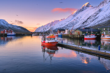 Wall Mural - red fishing boats on the sea, reflection in water, snowy mountains, colorful purple sky with pink cl