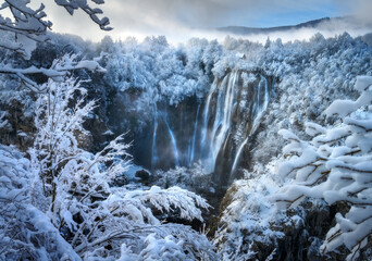 Wall Mural - aerial drone view of amazing waterfall and snowy forest at sunset. winter fairytale in plitvice lake