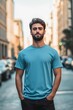 © Aleksander - A young man stands confidently in a city street, wearing a blue color T-shirt mockup and black pants. The background features blurred cars and buildings, creating an urban atmosphere.