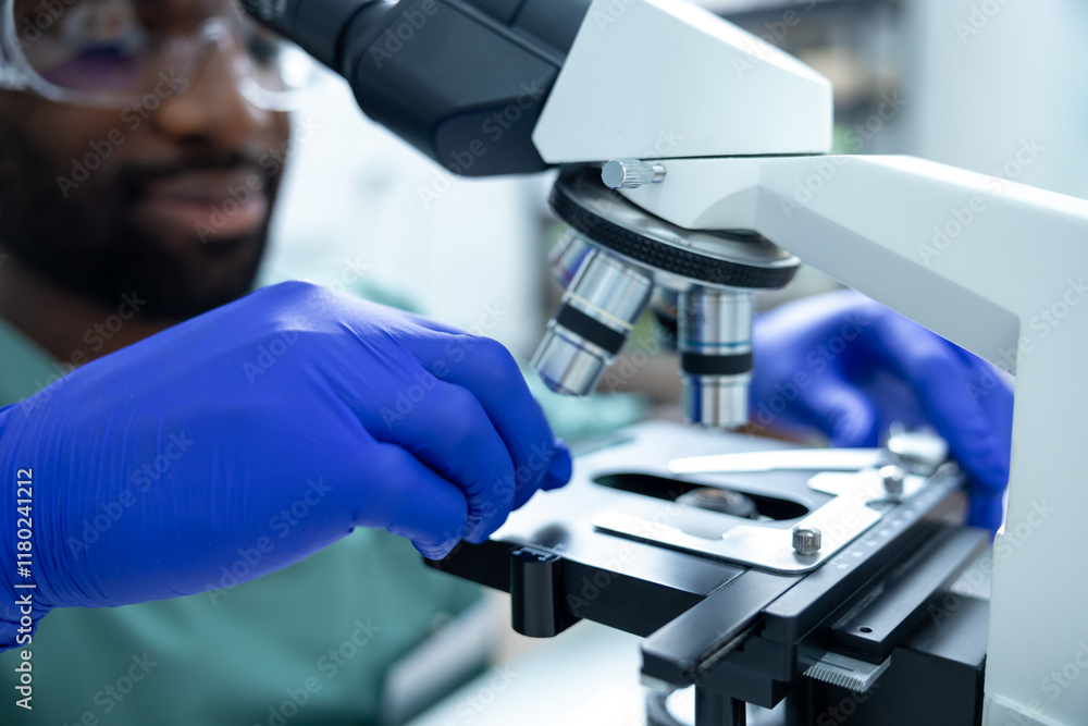 African American male scientist in lab using lens of microscope for ...