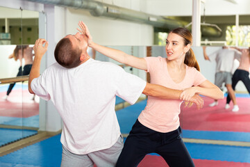 Wall Mural - Caucasian woman performing chin strike while sparring with man in gym during self-defence training.