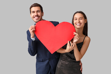 Wall Mural - Beautiful young couple with red paper heart on grey background. Valentine's day celebration