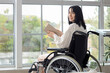 © Pixel-Shot - Beautiful young woman in wheelchair reading book at home