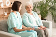 © Pixel-Shot - Young nurse with clipboard and senior woman sitting on sofa at home