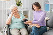 © Pixel-Shot - Senior woman in wheelchair with nurse measuring blood pressure at home