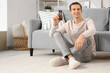 © Pixel-Shot - Young man with TV remote control sitting on floor at home