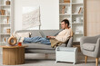 © Pixel-Shot - Young man using laptop on sofa with electric convector heater at home