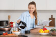 © Pixel-Shot - Young woman with newspaper pouring coffee while frying vegetables in kitchen