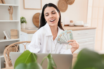 Wall Mural - Beautiful woman with dollar banknotes using laptop at table in kitchen