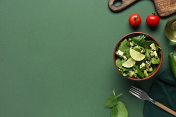 Bowl of tasty avocado salad with spinach leaves and lime on green background