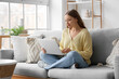 © Pixel-Shot - Beautiful young woman using laptop while sitting on sofa in living room