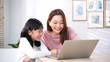 © bixpicture - Mother and Daughter Smiling and Using Laptop Together at Home. Family Bonding, Online Learning, Lifestyle or Entertainment in Comfortable Living Room.