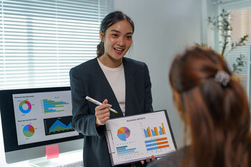 Sticker - Smiling businesswoman holding business reports and explaining charts and graphs to her colleague during a meeting in a modern office, fostering collaboration and strategic planning