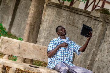 African American man seated in the garden calmly using phone for leisure, Technology, game, gamer, gaming, connection