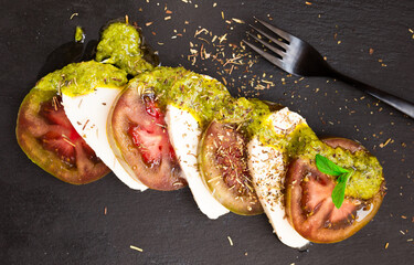 Wall Mural - Caprese salad with mozzarella, black tomatoes and pesto on black stone plate