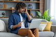 © Liubomir - Disappointed and deceived man sitting on sofa in living room with laptop and bank credit card in hands. Received a refusal to transfer funds, account blocking, and fraudulent actions.