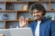 © Liubomir - Man at home on sofa using laptop for video call, young student waving happily at online conference meeting.