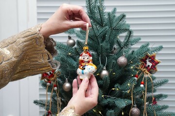 Hands of European woman in gold sweater hanging vintage nutcracker figurine on Christmas tree branches as decoration for winter holidays