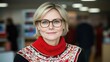© imagineRbc - A woman wearing glasses and a red sweater is smiling. She is standing in a room with other people