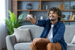 © Liubomir - Joyful man turns on the air conditioner, sits with the remote control in his hands from the smart home system, on the sofa in the living room at home.