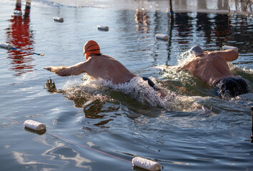 Wall Mural - Two men are swimming in a lake, one of them is wearing a red and orange swim cap