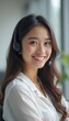 © natakot - A cheerful young woman with long, wavy hair wears a headset, radiating positivity in a modern office setting. Her warm smile and professional attire create an inviting atmosphere, perfect for customer