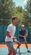 © natakot - Two young men, one in a white shirt and the other in a dark blue shirt, are engaged in an intense tennis match on a sunlit court. The focus and determination on their faces highlight the competitive